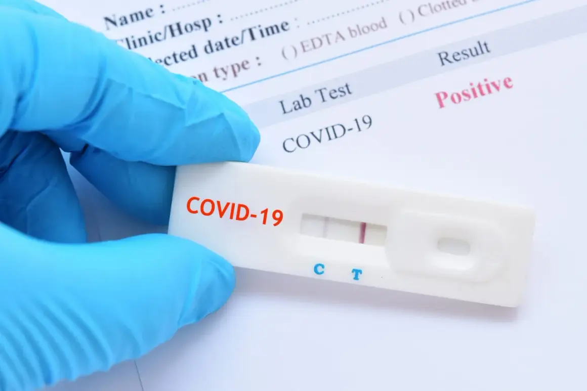 Ręka w niebieskiej rękawiczce trzyma test antygenowy COVID-19 z dwoma widocznymi paskami, wskazującymi na pozytywny wynik.