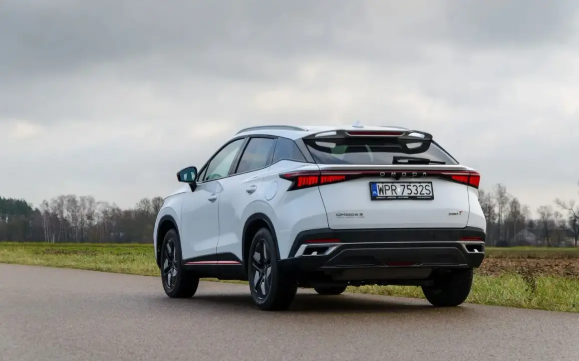 Białe, nowoczesne chinskie auto OMODA 5 z charakterystycznym pasem świateł z tyłu, zaparkowane na poboczu drogi.