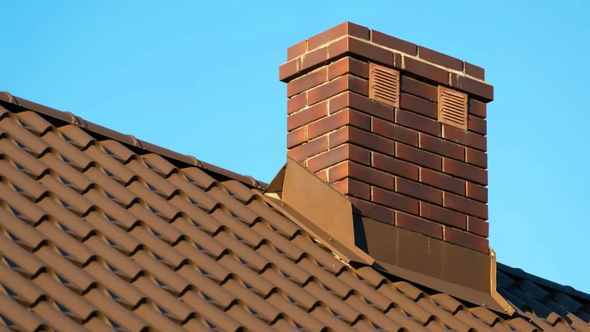 Ziegel-Schornstein auf braunem Ziegeldach vor blauem Himmel. Überlegungen, den alten Schornstein stilllegen zu lassen, sind im Gange.