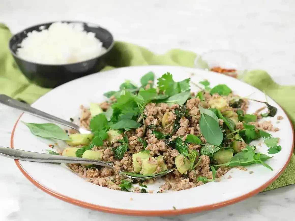 En tallrik med kycklingfärs, färska örter och grönsaker, perfekt för ett snabbt larb recept. Ris i bakgrunden.