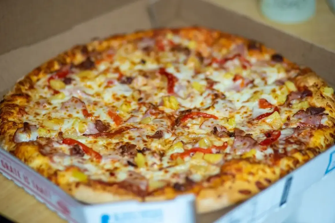 Pyszna pizza hawajska w pudełku, idealna do odgrzania w mikrofali. Ser, szynka i ananas kuszą swoim wyglądem.