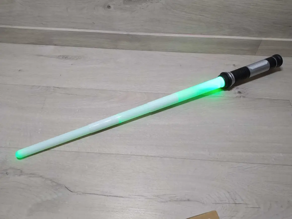 Zielony miecz Star Wars leży na drewnianej podłodze.