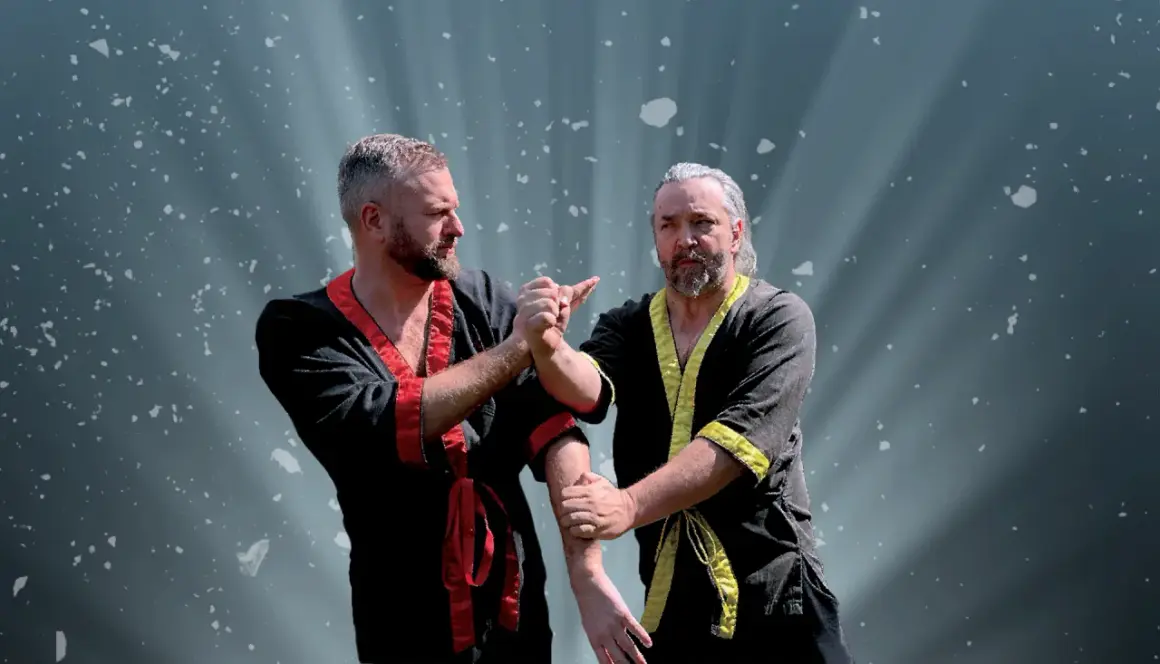 Två män i traditionella dräkter tränar wing chun. Ljuset strålar bakom dem.