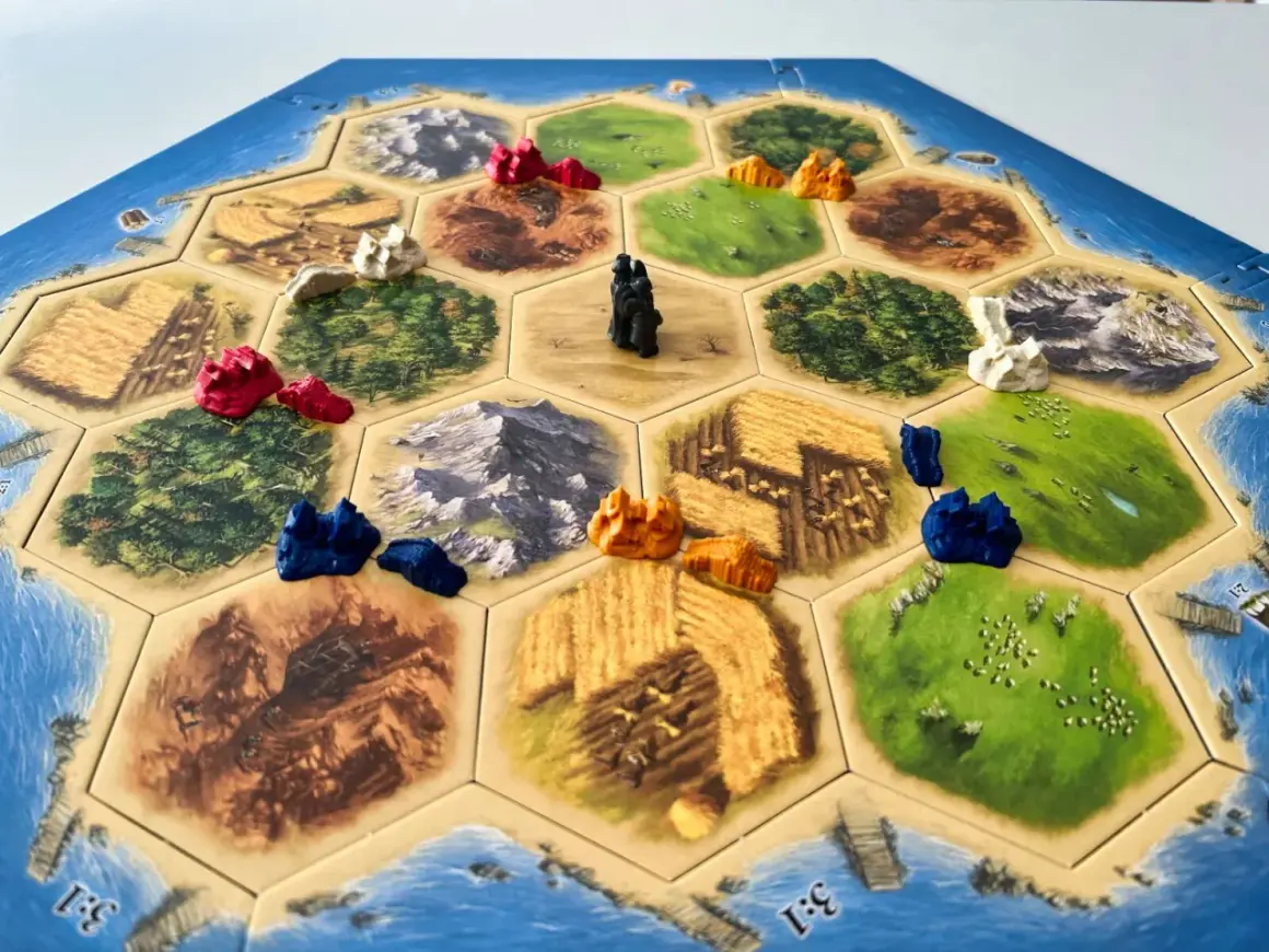 Plansza do gry osadnicy z Catanu, z pionkami i polami zasobów. Catan instrukcja w tle.