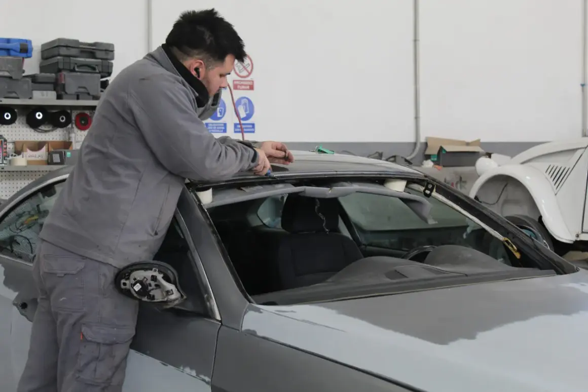 Taller mecánico. Un hombre trabaja en el techo de un coche gris, solucionando stage 1 problemas.