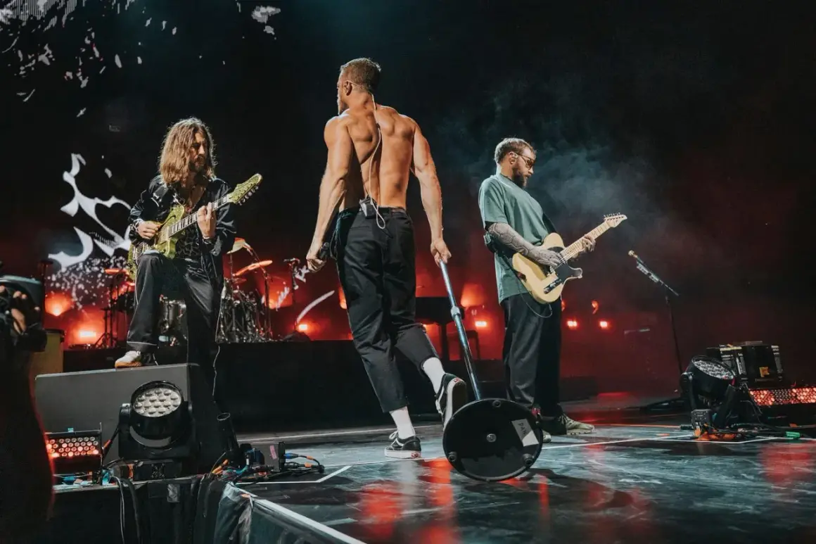 Imagine Dragons na koncercie w Polsce: wokalista bez koszulki, gitarzyści grający na scenie.
