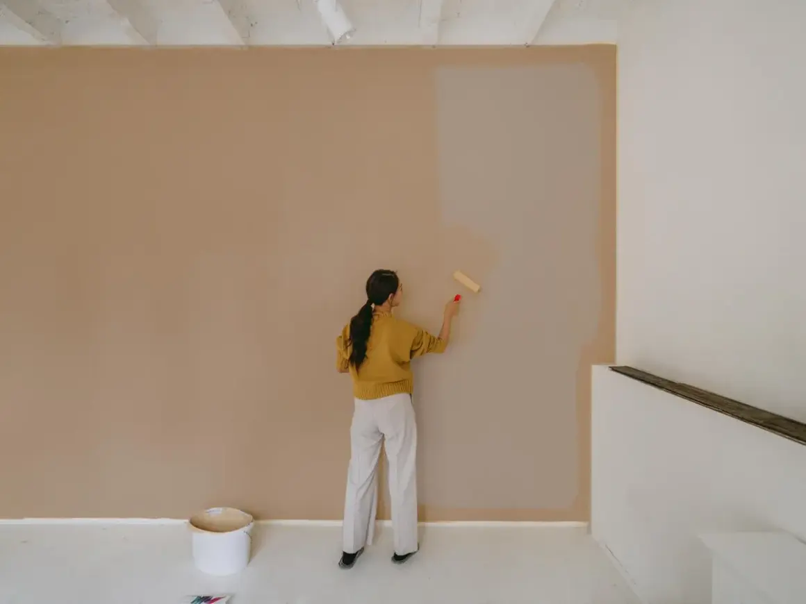Frau streicht Wand mit neuer Farbe. Die Frage, wie lange braucht Wandfarbe zum trocknen, beschäftigt sie.