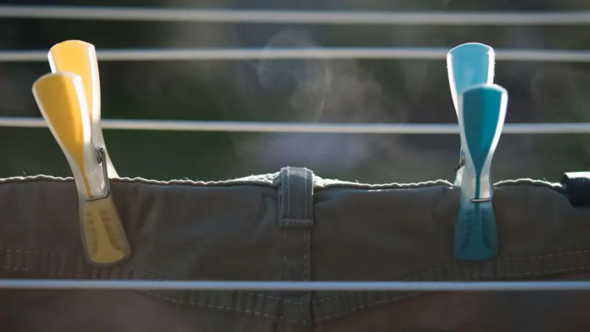 Zwei Wäscheklammern, gelb und blau, halten eine Hose auf einer Wäscheleine. Dampf steigt auf, die Hose trocknet schnell.