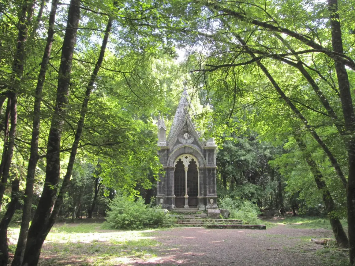 Un piccolo tempietto gotico nel **bosco delle fate a Torre Alfina**, circondato da alberi rigogliosi e sentieri ombrosi.