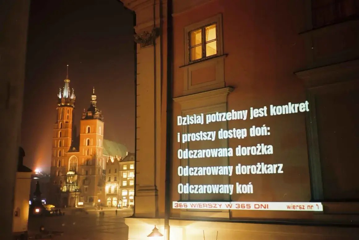 Nocny Kraków. Na ścianie budynku wyświetlane są wiersze o krakowie, m.in. o odczarowanej dorożce.