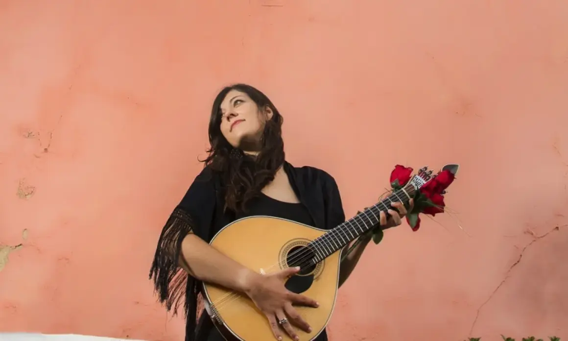 Młoda kobieta z gitarą, ozdobioną czerwonymi różami, przypomina duchem Amalię Rodrigues, legendę fado.