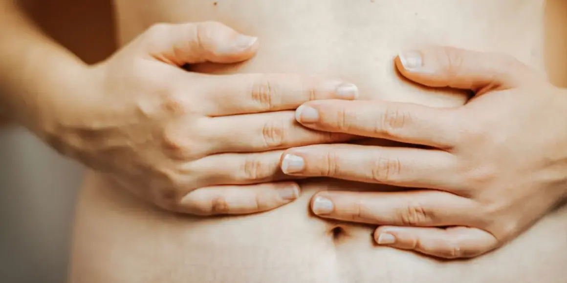 Mains d'une femme sur son ventre, évoquant la constipation et la pression sur la vessie.