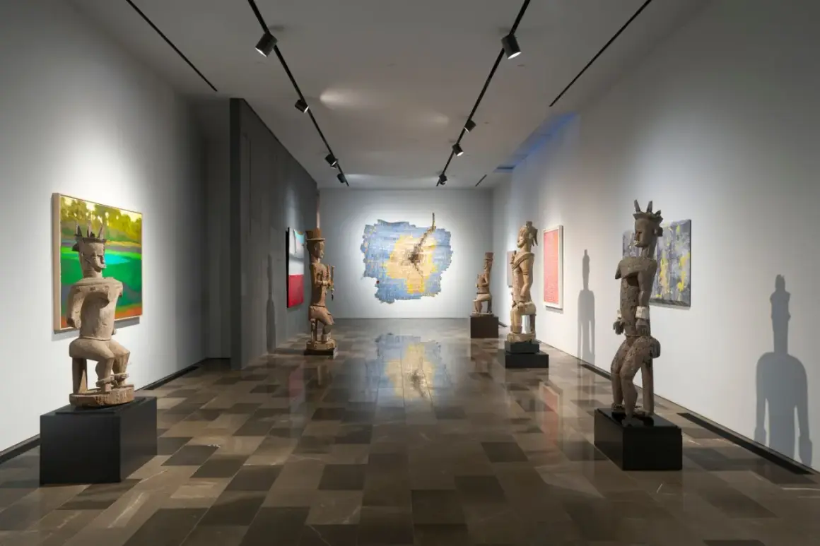 Osman Can Yerebakan's exhibition features striking wooden sculptures and vibrant paintings in a modern gallery space.