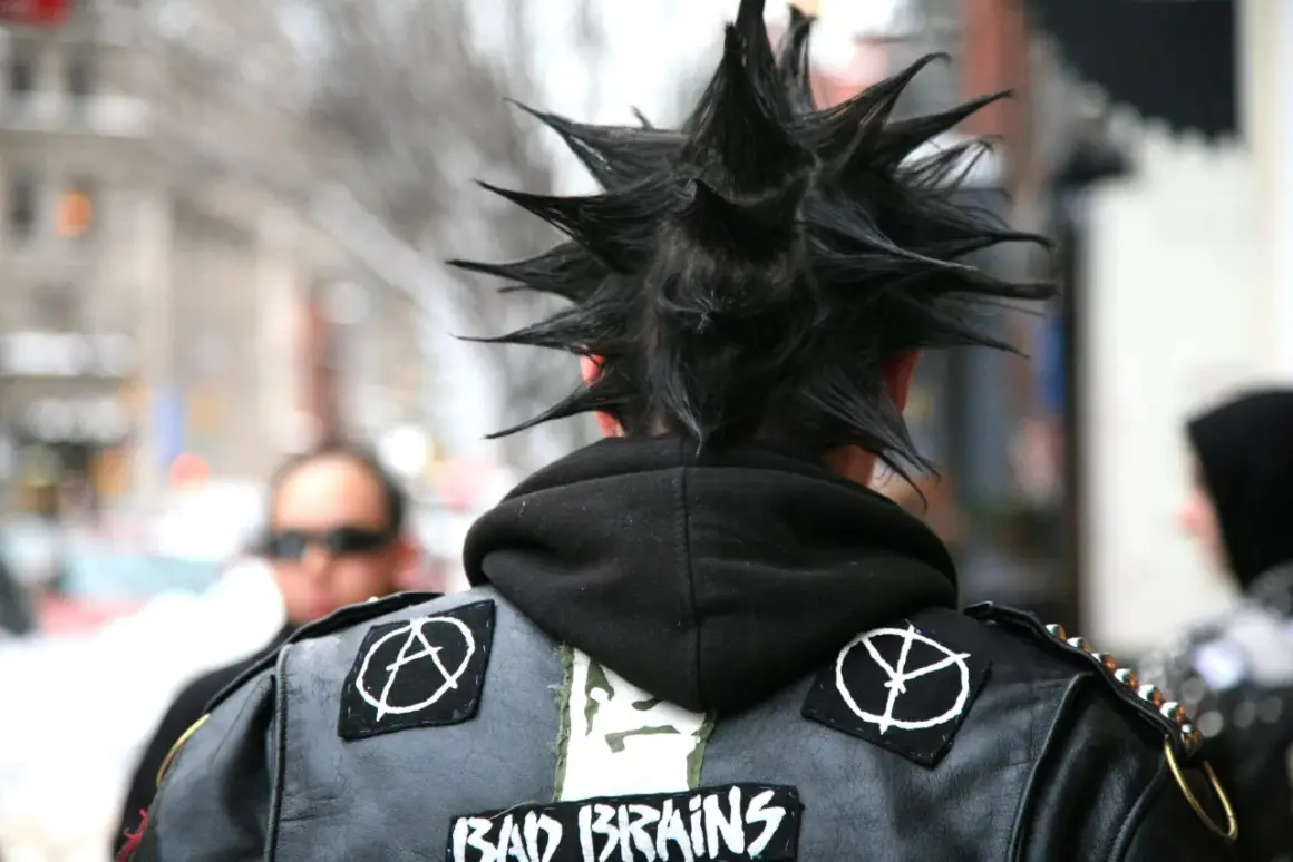 Un ragazzo con cresta punk e giacca di pelle con toppe, un'icona dei gruppi punk anni 2000.