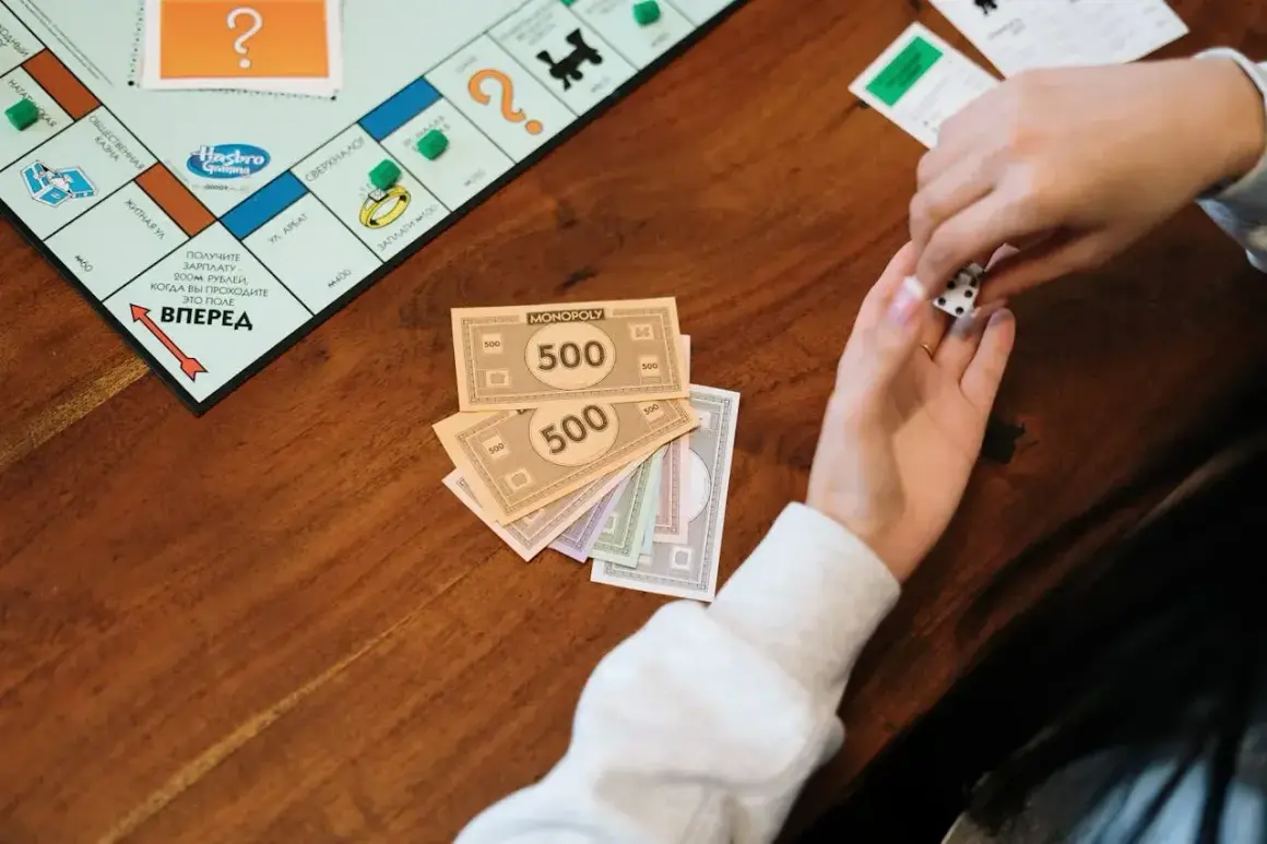 Ręce rzucają kostką do gry w Monopoly. Na stole leżą pieniądze z gry, symbolizujące eurobiznes i bogactwo.