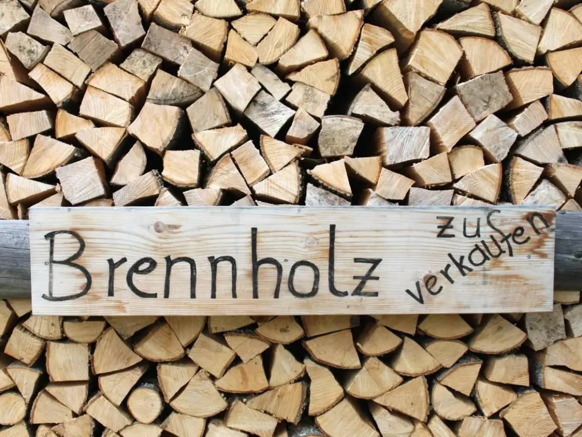 Holzstapel mit einem Schild "Brennholz zu verkaufen". Das Holz ist gespalten und bereit für den Winter, ob esche oder buche.