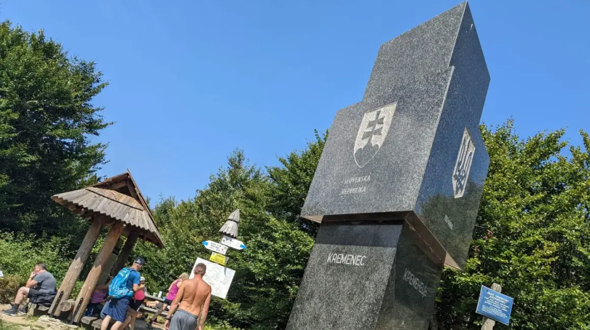 Trójstyk granic Bieszczady: monumentalny obelisk z herbami Słowacji i Ukrainy, otoczony zielenią.
