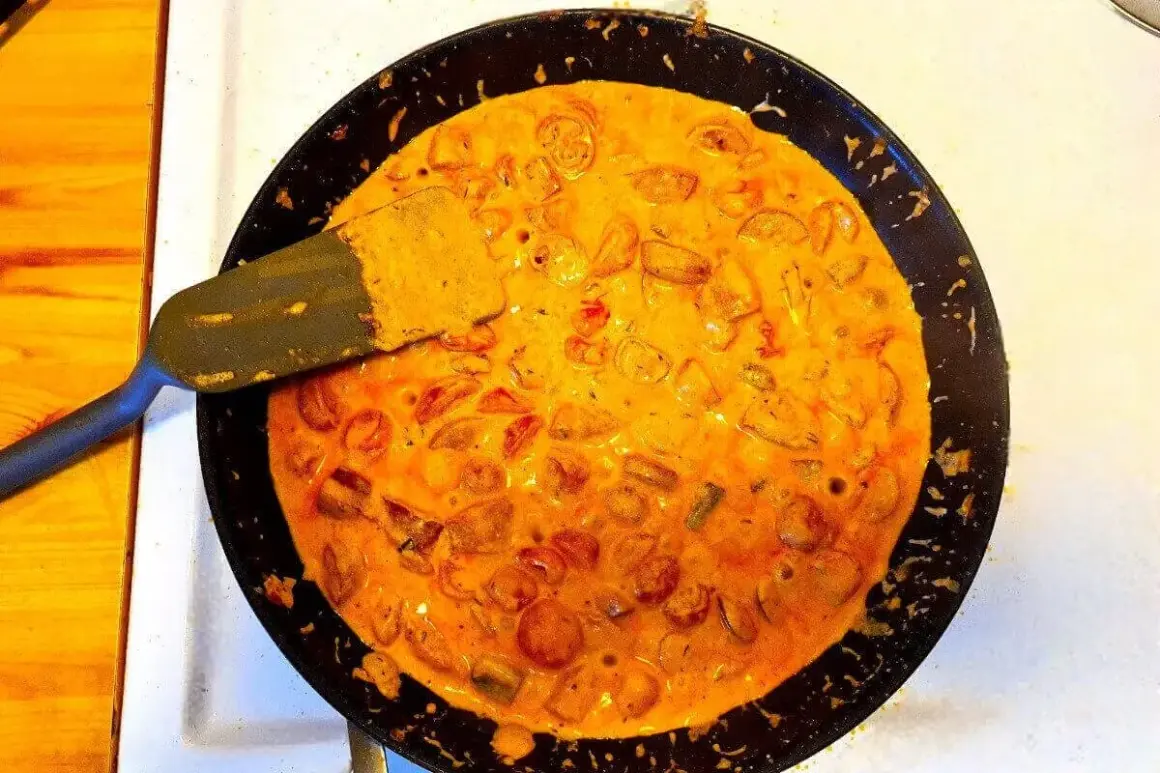 En stekpanna med krämig korv stroganoff bubblar. En spatel lyfter upp en bit av den läckra grytan.