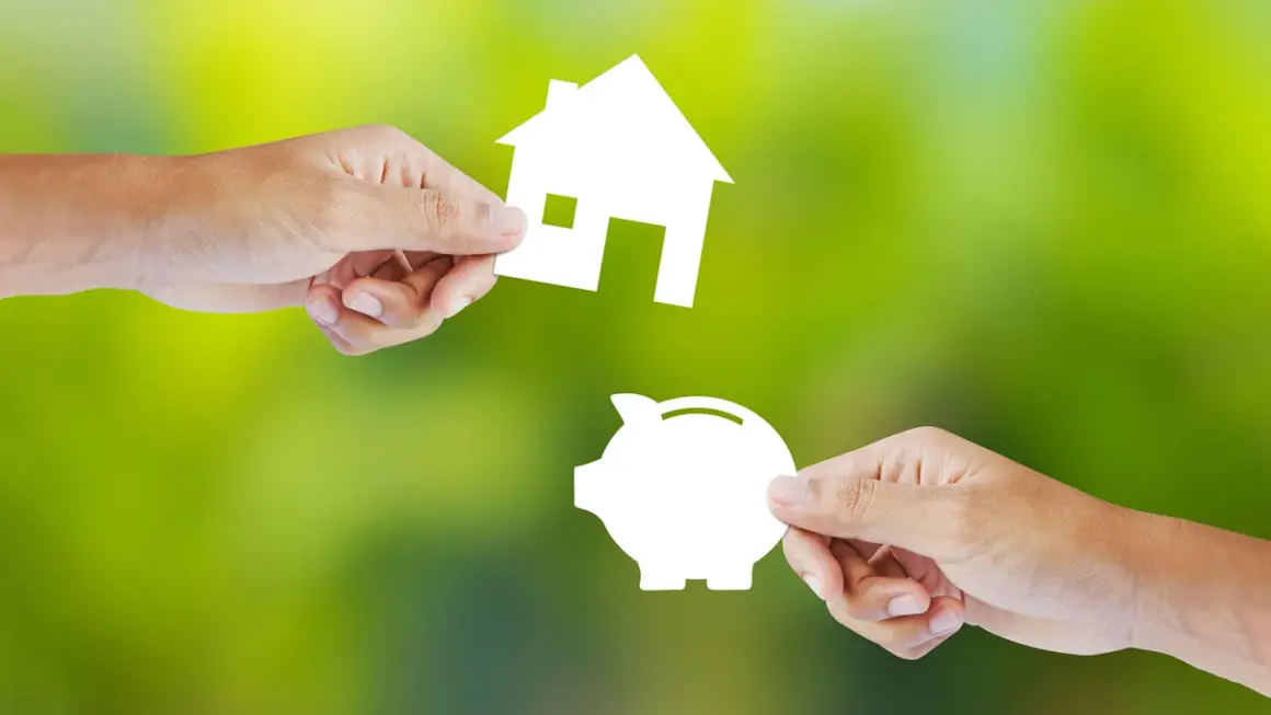 Manos intercambian una casa y una alcancía, simbolizando la decisión de alquilar o comprar.