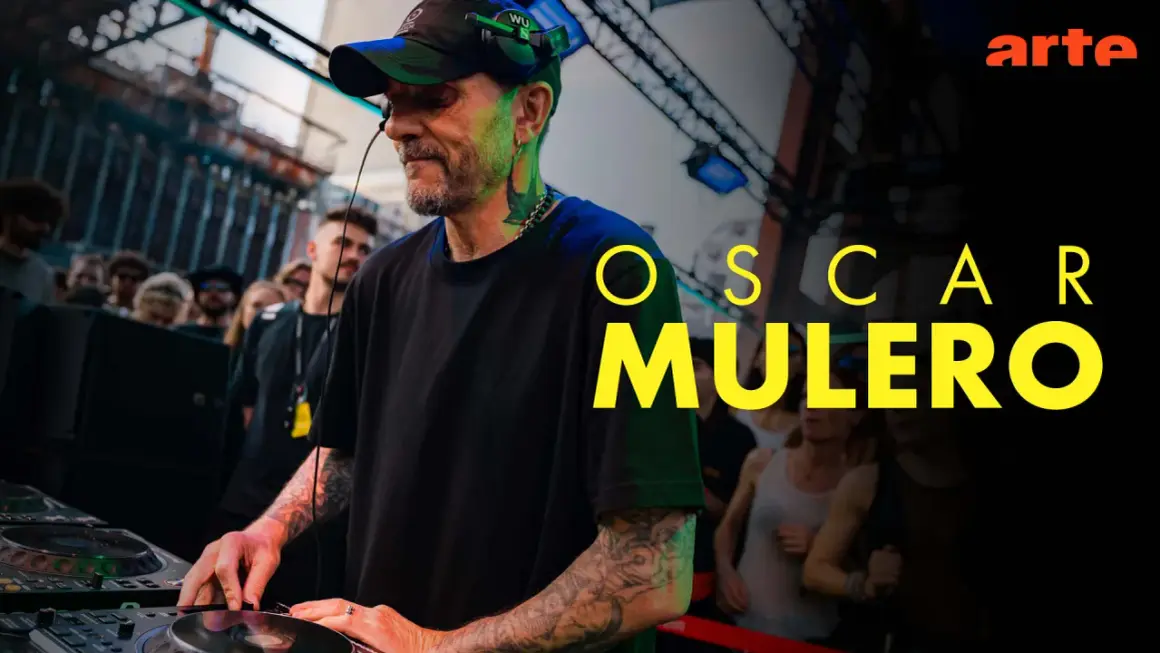 Oscar Mulero, DJ con cuffie e cappellino, mixa musica in un locale affollato. Il suo nome campeggia in giallo.