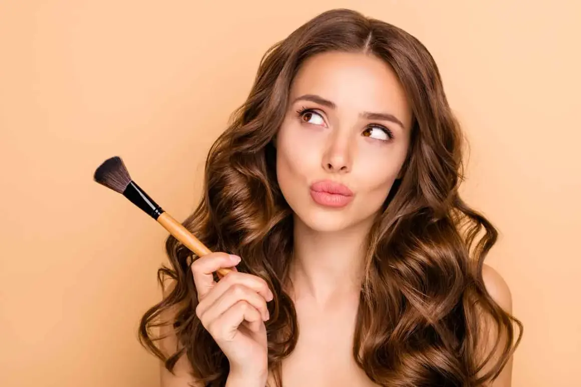 Ragazza con pennello da trucco, pensierosa, mentre impara a truccarsi.
