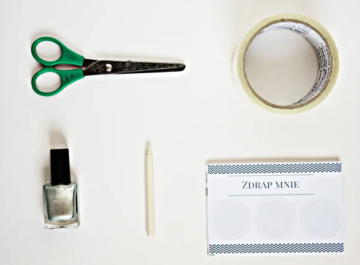 Potrzebne do zrobienia zdrapki DIY: nożyczki, srebrny lakier, taśma, biała kredka i kartka z napisem "ZDRAP MNIE".