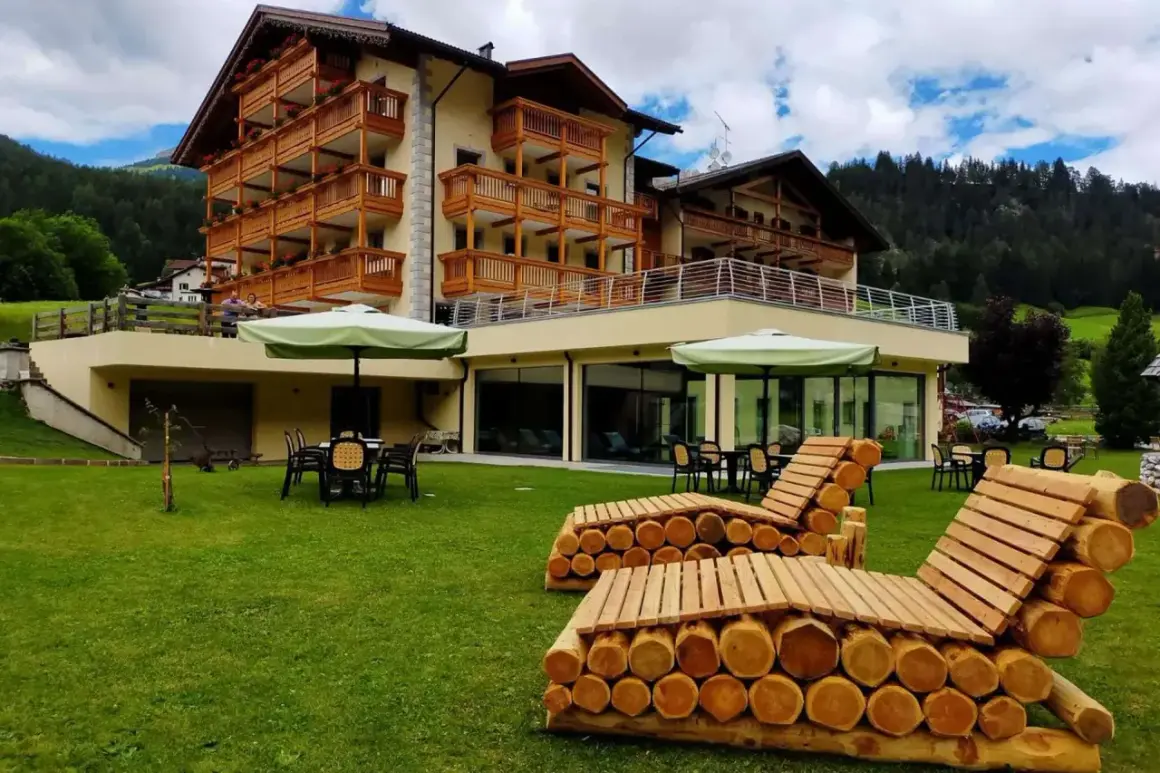 Hotel Dolomia Soraga: un'oasi di relax con vista sulle montagne. Panchine in legno e prato verde invitano al riposo.