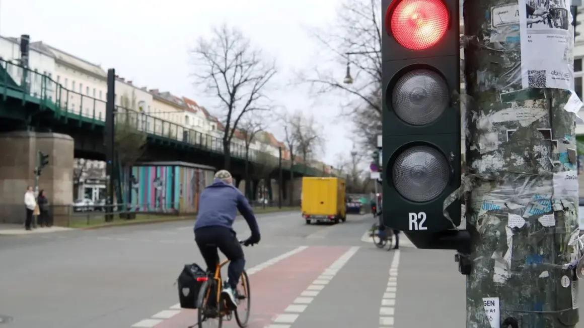 Ein Radfahrer wartet an einer roten Ampel. Im Hintergrund eine gelbe LKW und eine Hochbahn.