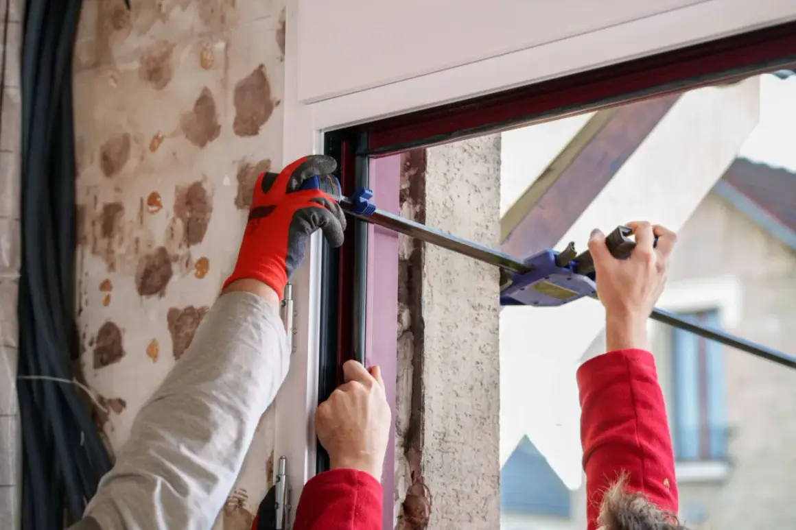 Pose d'une porte d'entrée sur dormant existant. Un ouvrier utilise un serre-joint pour ajuster le cadre.