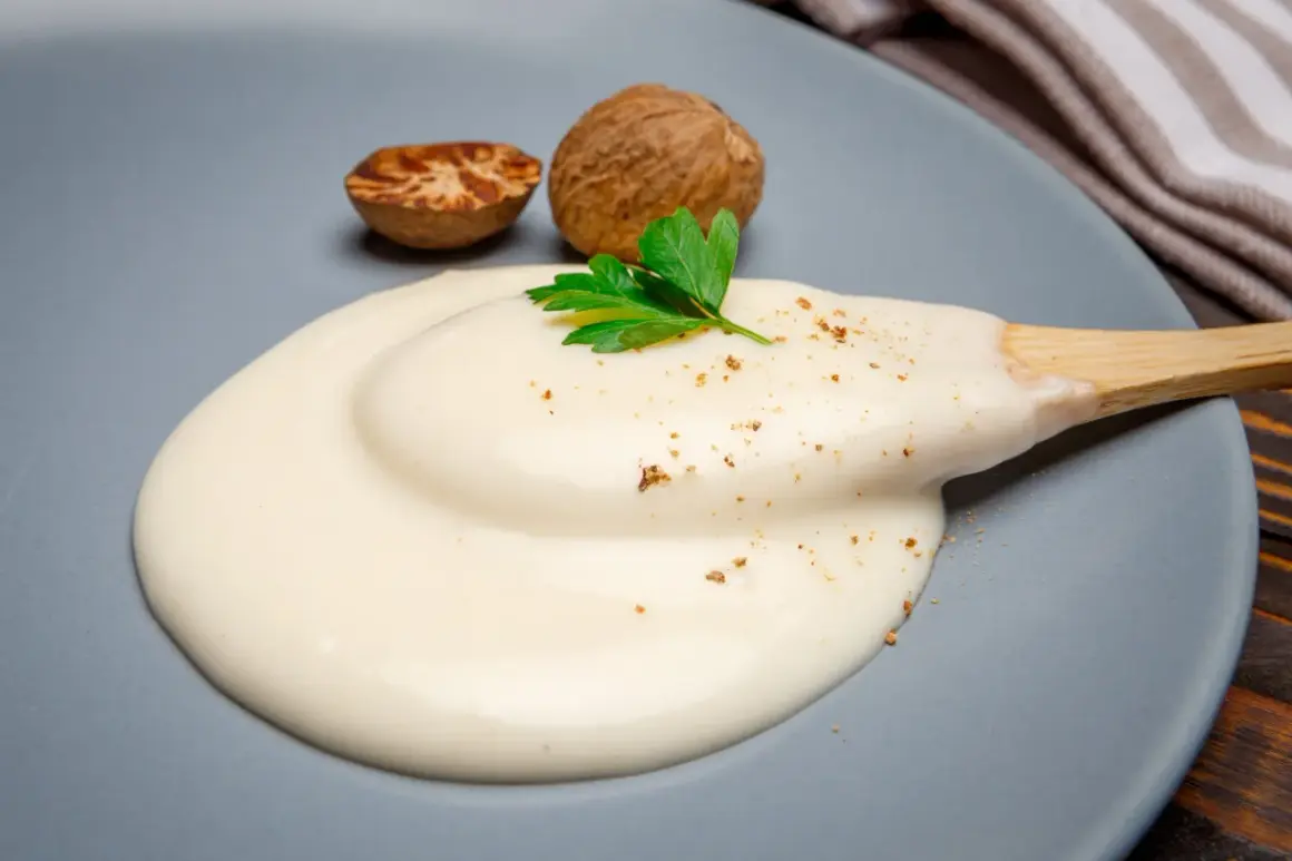 Krämig bechamelsås på en tallrik med muskotnötter och persilja. Perfekt för ditt bechamelsås recept.