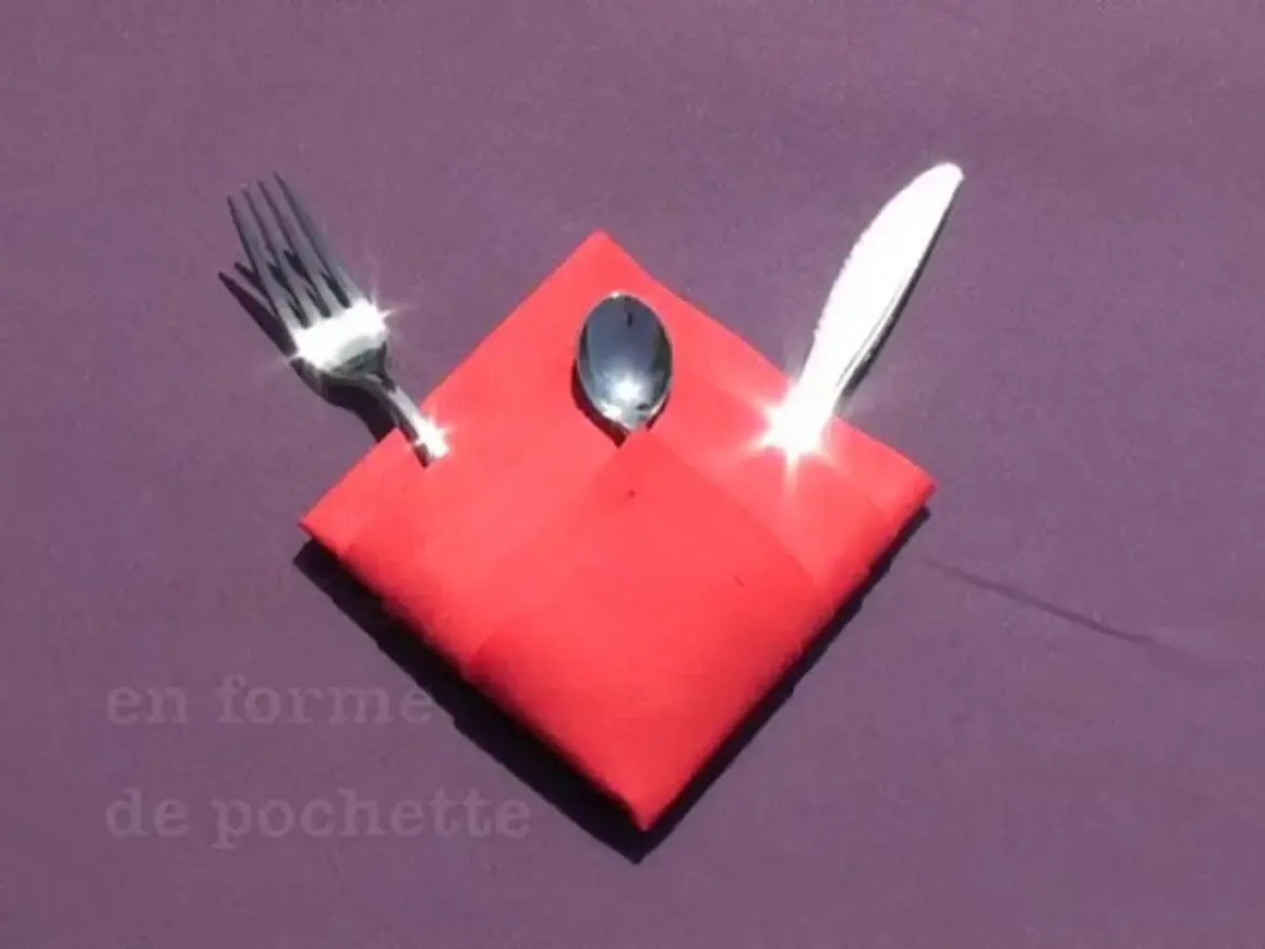Pliage serviette Noël porte couvert en forme de pochette rouge, avec une fourchette, une cuillère et un couteau.