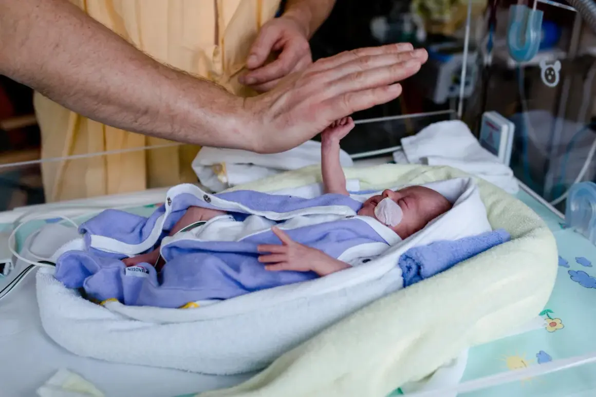 Dłoń ojca czule dotyka maleńkiego noworodka z hipotrofią, otulonego w kocyki w inkubatorze.