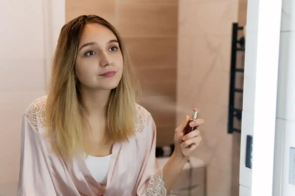 Młoda kobieta w szlafroku rozpyla perfumy. W powietrzu unosi się subtelny paczula zapach, otulając ją delikatną mgiełką.