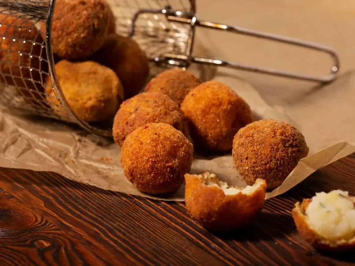 Croquetas de patata y pollo doradas y crujientes, algunas en una cesta metálica, otras sobre papel de estraza.