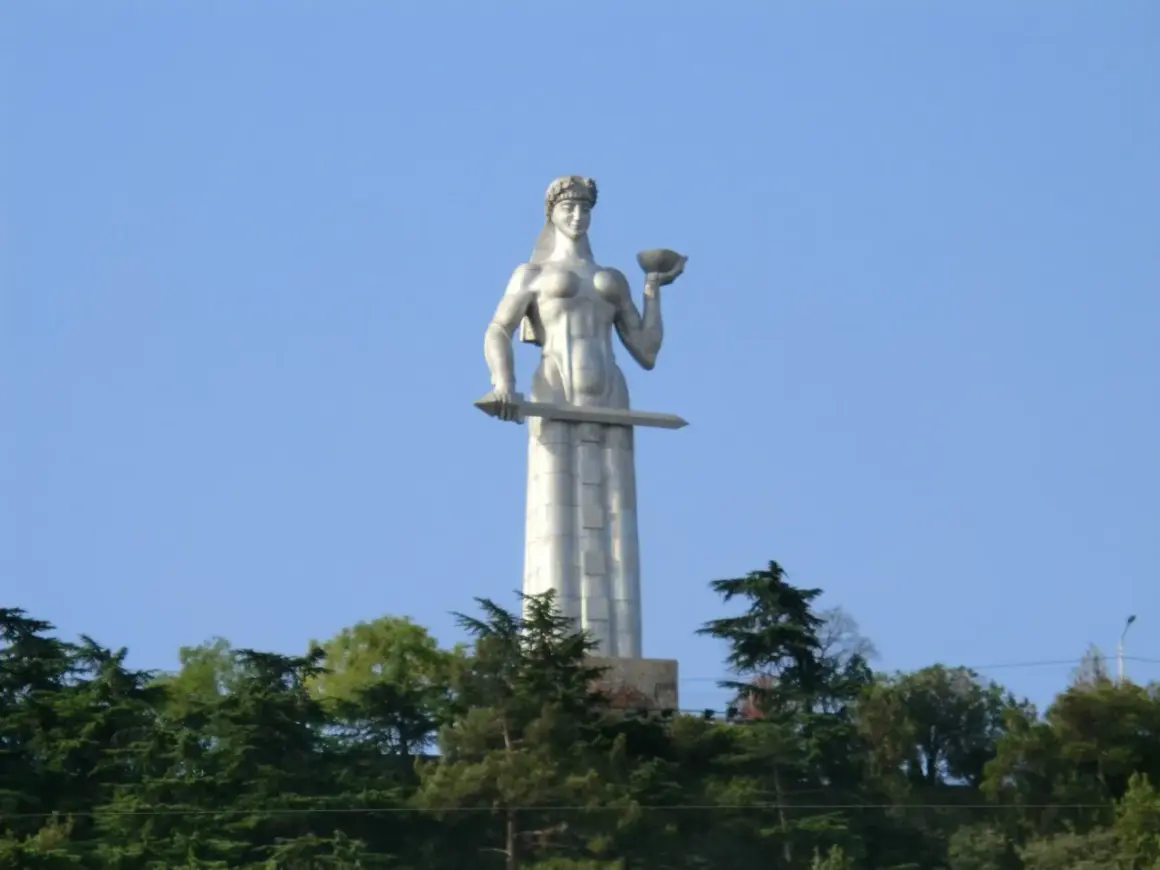 Matka Gruzja, symbol Tbilisi, trzyma miecz i puchar. Monumentalna postać wznosi się nad zielenią.
