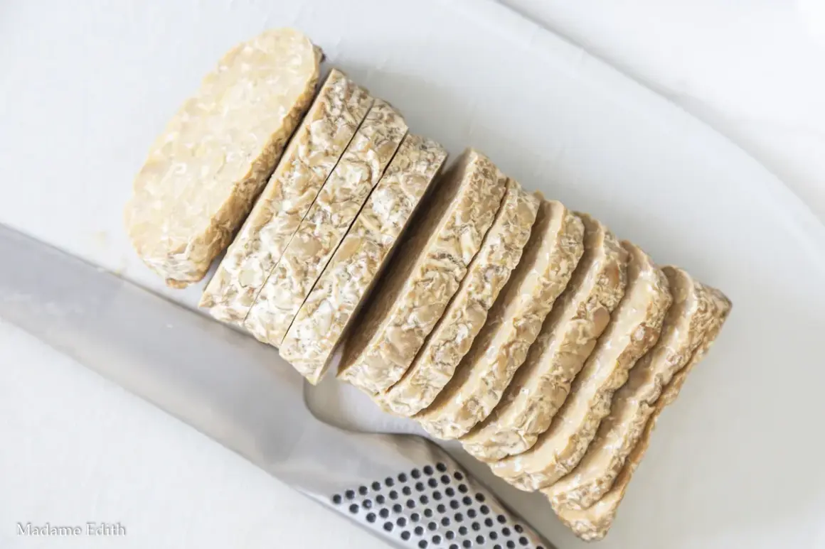 Pokrojony w plastry tempeh, czyli fermentowana soja, leży obok noża. To świetny składnik do wegańskich dań.