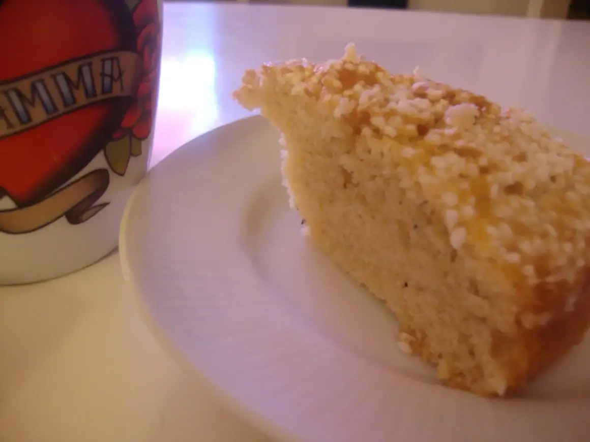 En bit gammaldags kardemummakaka med nötter på en vit tallrik, bredvid en mugg med texten "MAMMA".