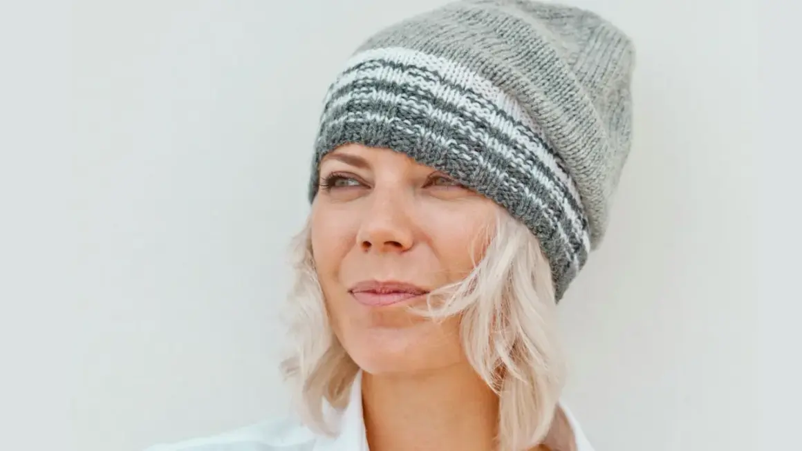 Frau mit blonden Haaren und Strickmütze, die nachdenklich in die Ferne blickt. Sie genießt ihr Leben mit 55 in Rente.