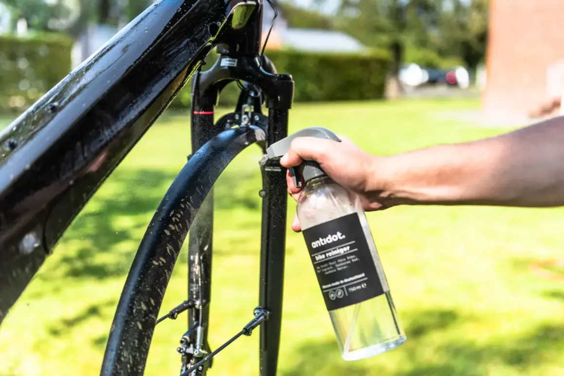 Hand sprüht Fahrradrahmen mit Reiniger ein. Sorgfältige Fahrrad Pflege für glänzende Ergebnisse im Freien.