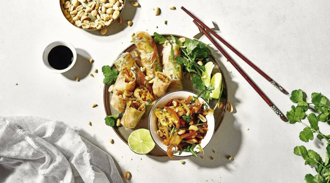 Frühlingsrollen mit Erdnüssen, Limette und Koriander – ein typisch asiatisches Essen, serviert mit Sojasauce und Stäbchen.