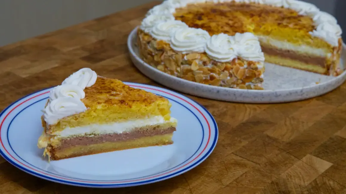Un trozo de tarta o pastel de capas con crema y almendras, coronado con nata montada.