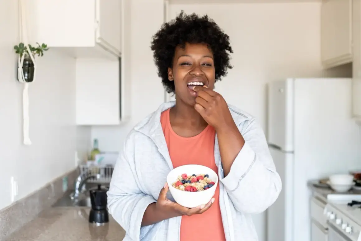 Une femme savoure un bol de céréales et de fruits, un exemple d'alimentation intuitive.