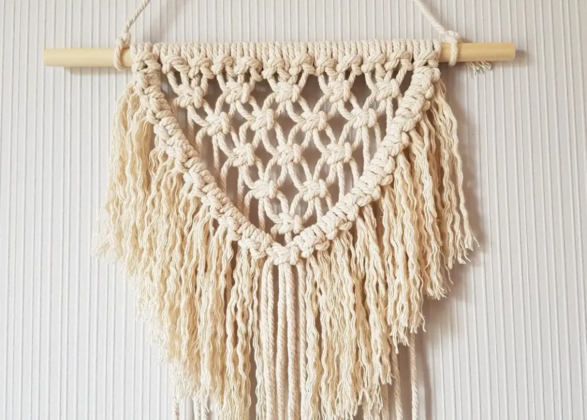 Un joli macramé tuto, suspendu à une tige de bois, avec des franges douces et un motif en losanges.