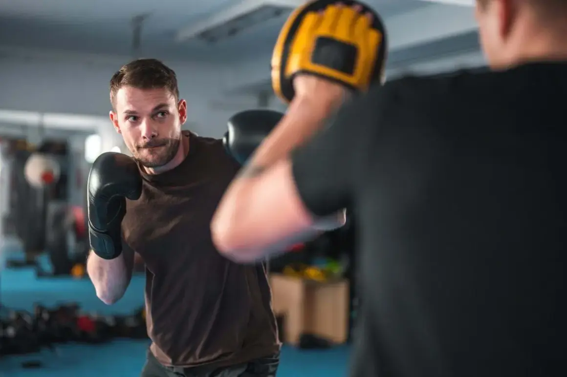 A man in black boxing gloves practices his boxing workout routine, focusing on his opponent holding a yellow mitt.