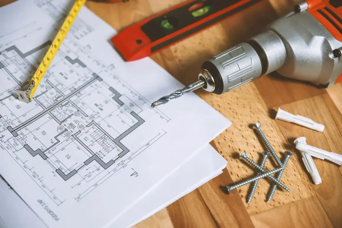 Plan de maison, mètre, vis, chevilles et perceuse de la marque Einhell, prêts pour le bricolage.