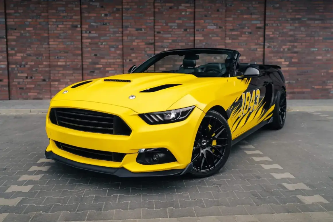 Żółty kabriolet Mustang z czarnymi akcentami i grafiką "1849" na boku. Wygląda jak model z 2026 roku, gotowy na podbój dróg.