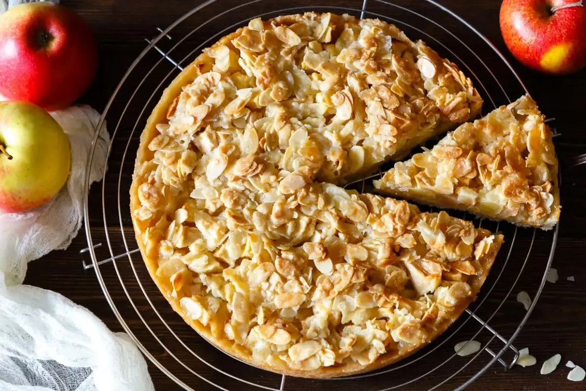 Ein goldbrauner florentiner apfelkuchen mit knusprigen Mandelblättchen, daneben Äpfel und ein Stück Kuchen.