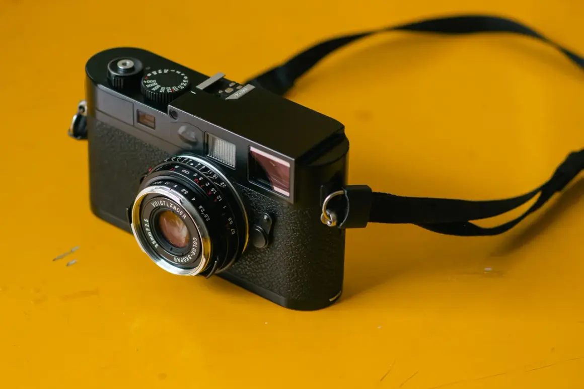 A black camera with a Voigtlander Color Skopar 35mm lens sits on a yellow surface.
