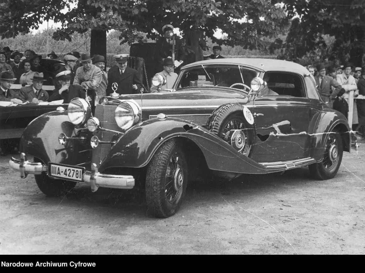 Elegancki, zabytkowy pierwszy mercedes z lat 30. XX wieku, z widoczną tablicą rejestracyjną IIA-42781, otoczony przez ludzi.