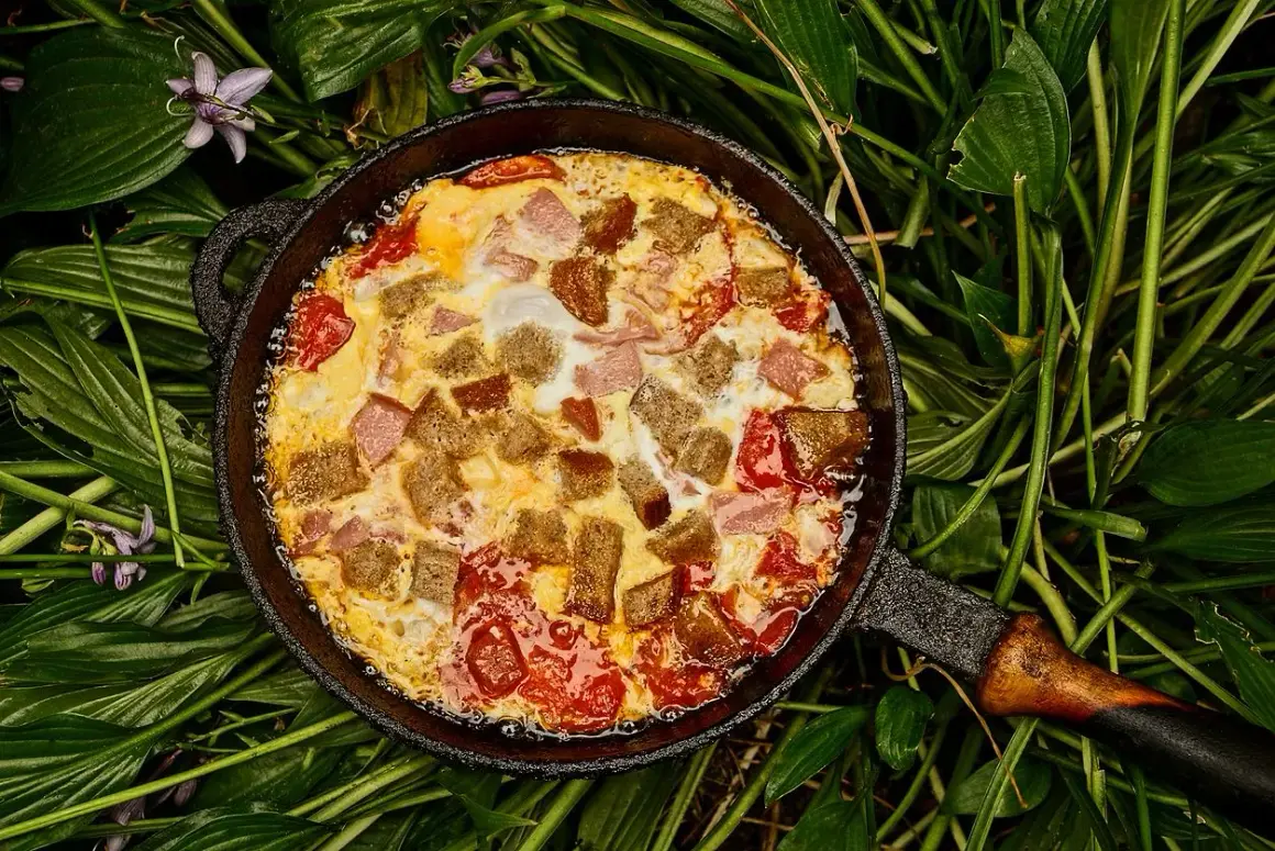 Pyszna kolacja z jajek z pomidorami i grzankami w żeliwnej patelni, otoczona zielonymi liśćmi.